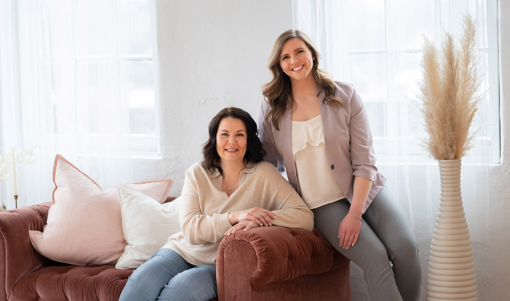 Becca and Michelle, owners of Creekside Hearing sitting on a couch smiling!